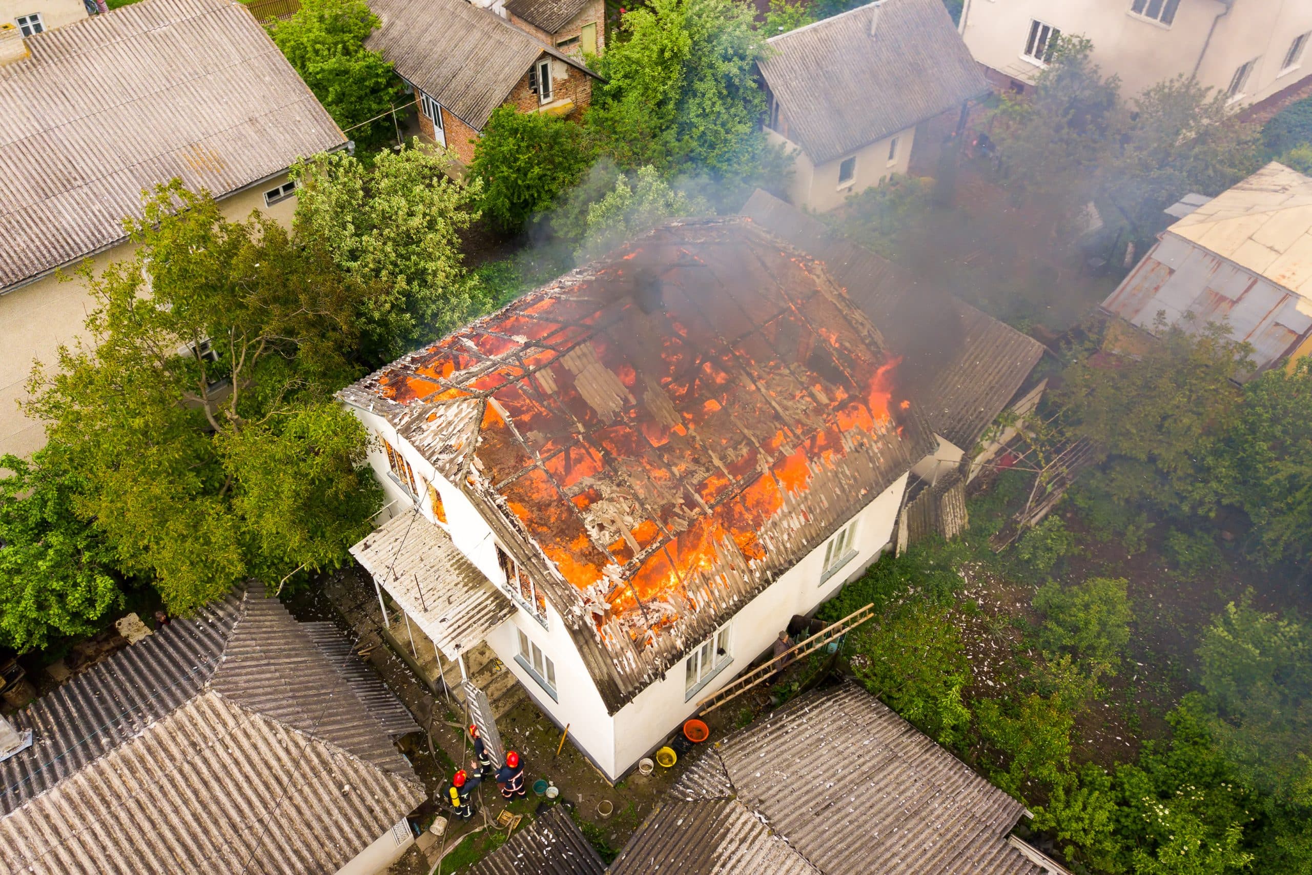 aerial view of a house on fire with orange flames and white thick smoke.