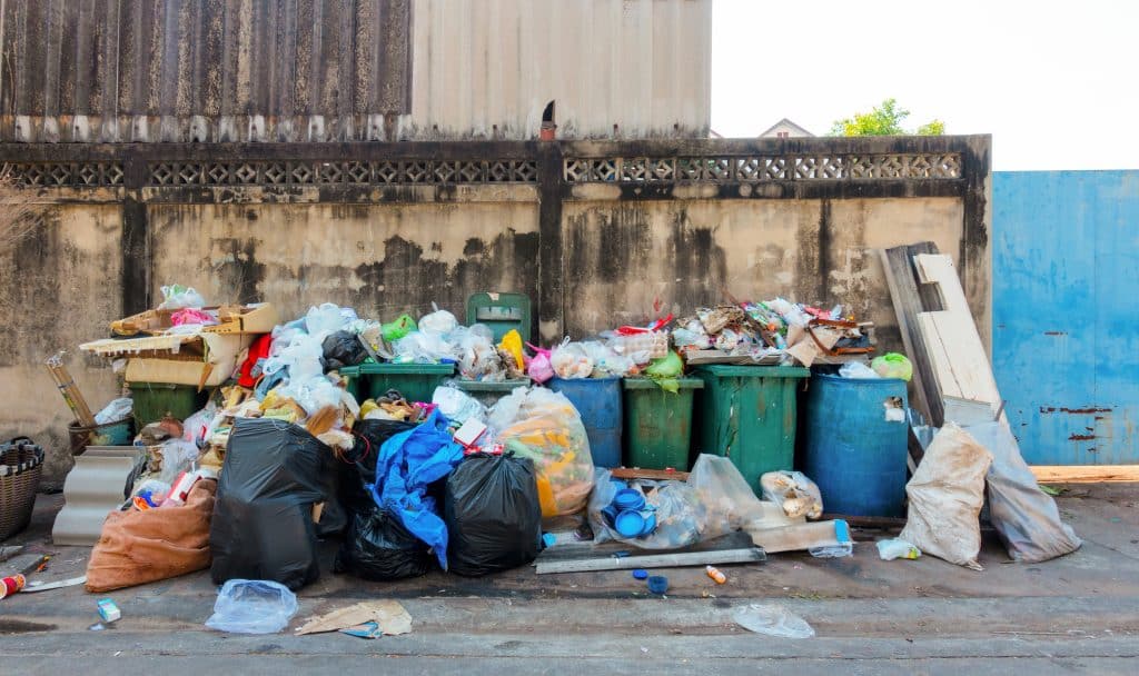 stack of different types of large garbage dump, plastic bags, and trash bins near a wall in urban area in environmental pollution concept in bangkok city, thailand