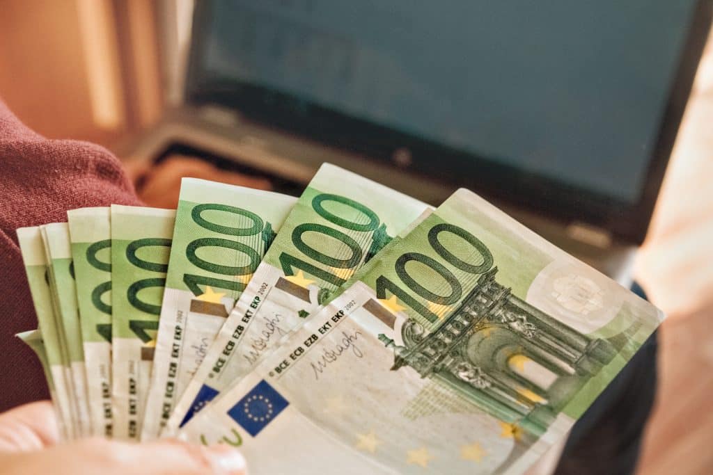 one hundred euro banknotes in palms of man on background of laptop with table on screen, slective focus, film noise